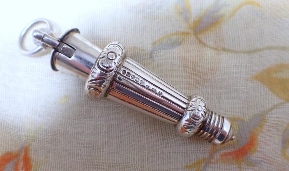 An ornate antique Edwardian sterling silver whistle pendant featuring engraved floral motifs, fluted detailing, and visible English silver hallmarks. View III