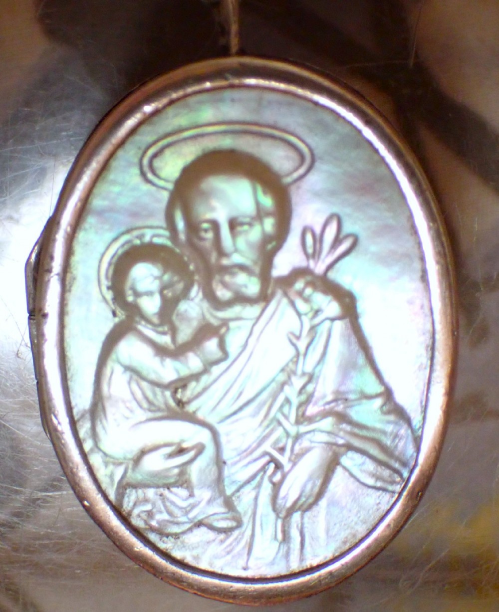 An oval Edwardian silver locket featuring a carved mother of pearl relief depicting Saint Christopher carrying the Christ child.
