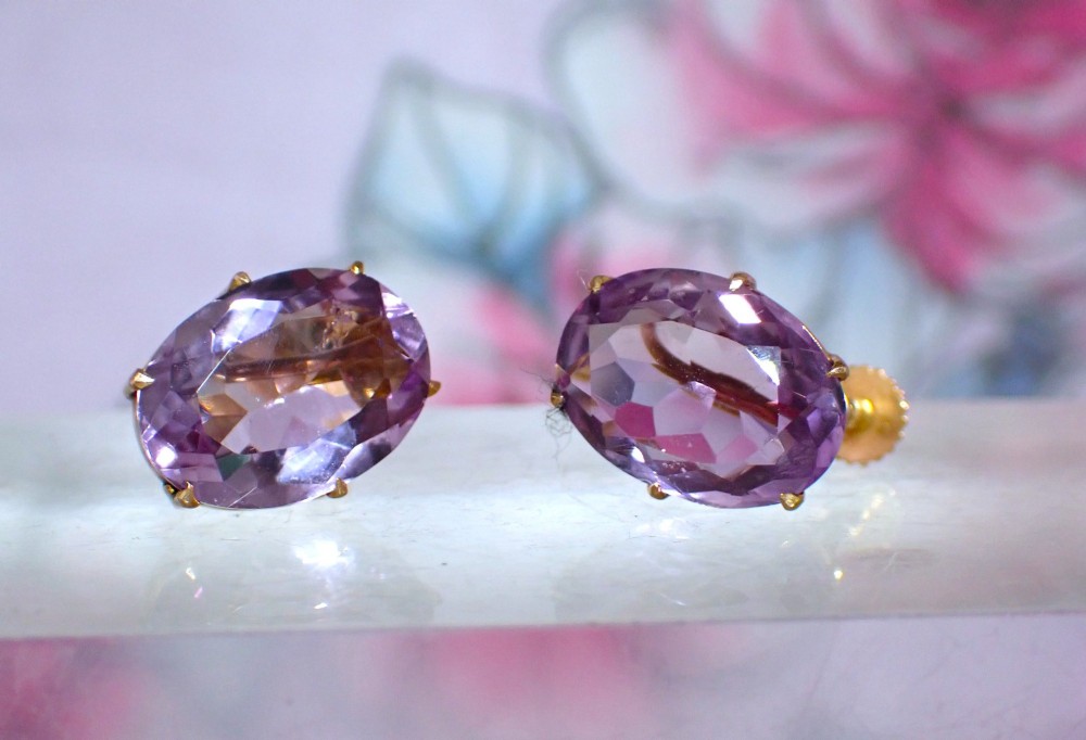 A pair of Edwardian 9ct yellow gold stud earrings set with oval faceted light purple amethyst gemstones and screw-back fastenings.