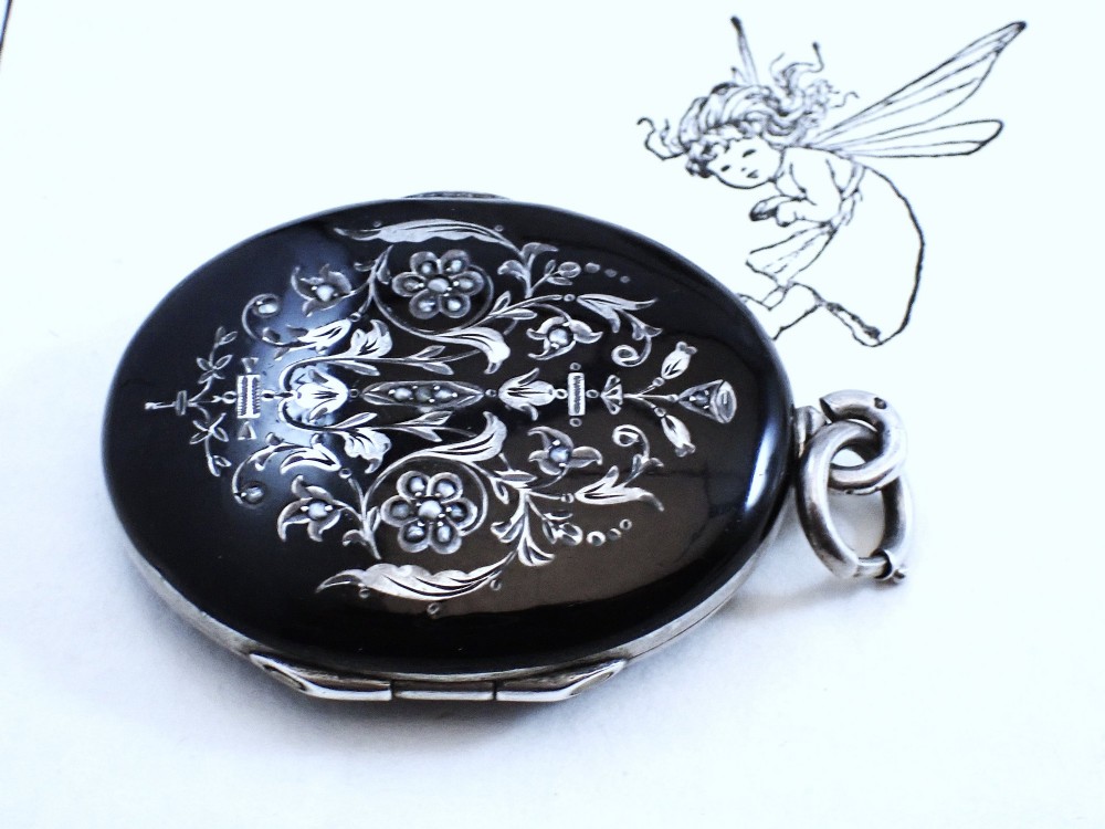 An oval Victorian black enamel locket with silver foliate inlay set with seed pearls, featuring a silver suspension bail. View IV