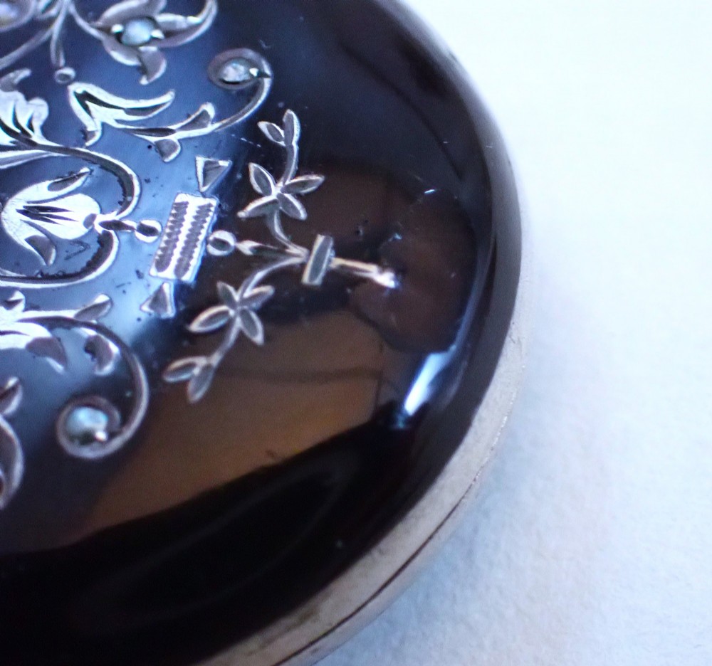 An oval Victorian black enamel locket with silver foliate inlay set with seed pearls, featuring a silver suspension bail. View V