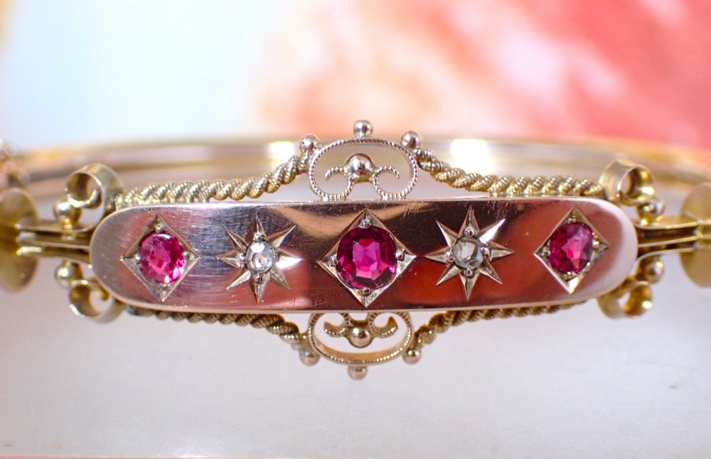 An Edwardian 9ct gold hinged bangle featuring three star-set rubies and two star-set diamonds set in an elongated panel with ropework borders.