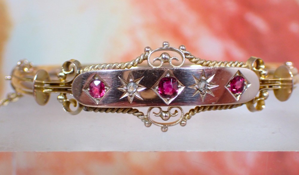 An Edwardian 9ct gold hinged bangle featuring three star-set rubies and two star-set diamonds set in an elongated panel with ropework borders. View II