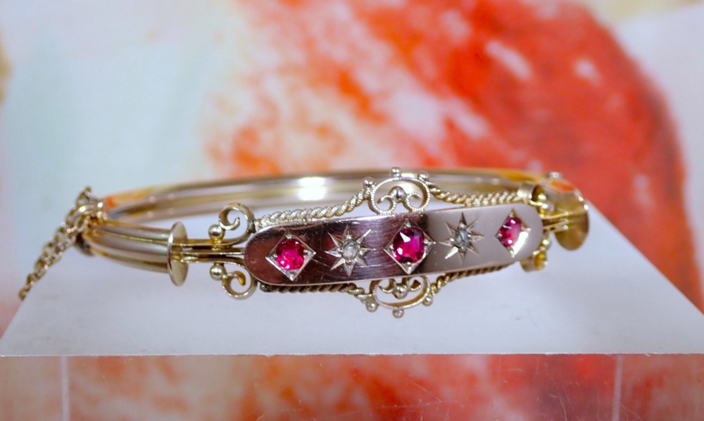 An Edwardian 9ct gold hinged bangle featuring three star-set rubies and two star-set diamonds set in an elongated panel with ropework borders. View III