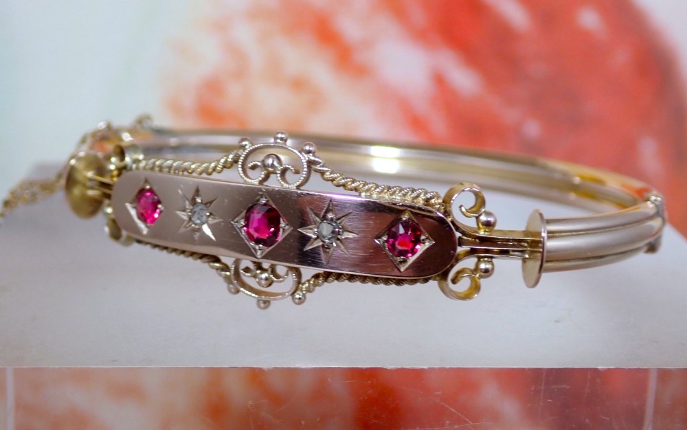 An Edwardian 9ct gold hinged bangle featuring three star-set rubies and two star-set diamonds set in an elongated panel with ropework borders. View IV
