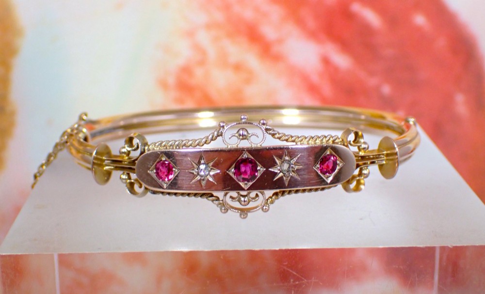 An Edwardian 9ct gold hinged bangle featuring three star-set rubies and two star-set diamonds set in an elongated panel with ropework borders. View V