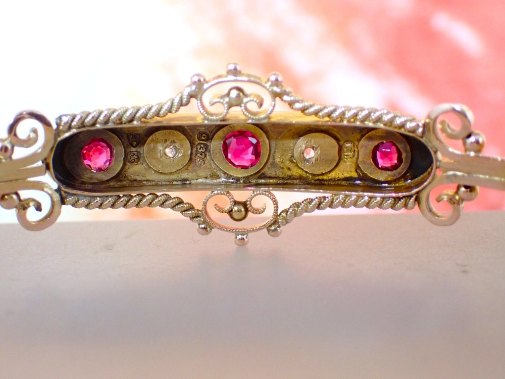 An Edwardian 9ct gold hinged bangle featuring three star-set rubies and two star-set diamonds set in an elongated panel with ropework borders. View VI