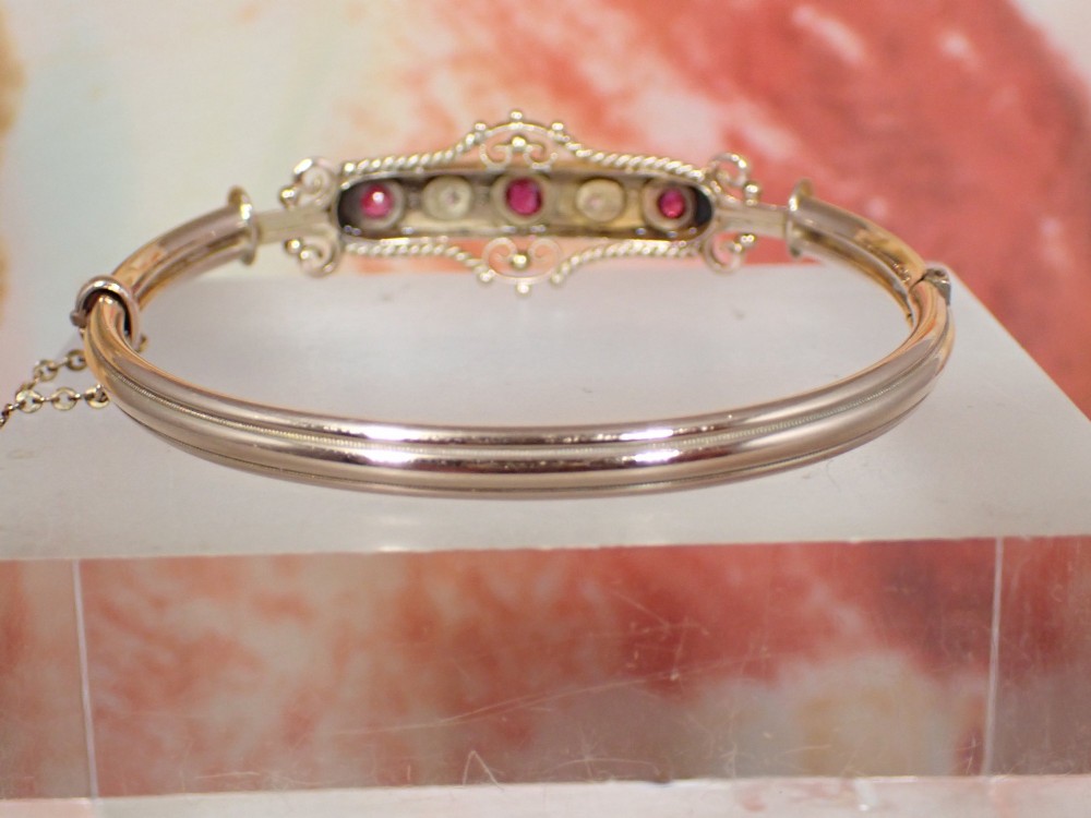 An Edwardian 9ct gold hinged bangle featuring three star-set rubies and two star-set diamonds set in an elongated panel with ropework borders. View VIII