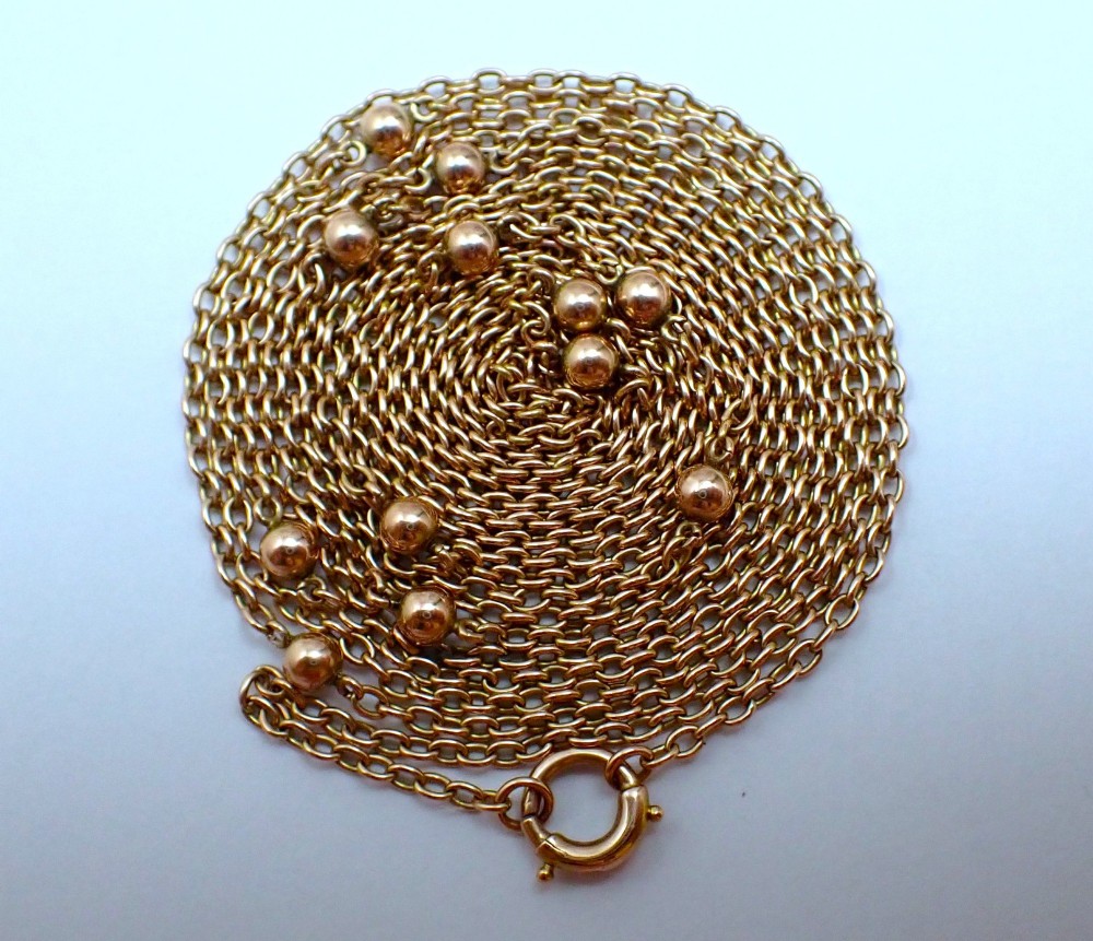 An antique Edwardian 15ct yellow gold guard chain coiled in a spiral, featuring small polished gold beads spaced along trace links and a spring ring clasp.