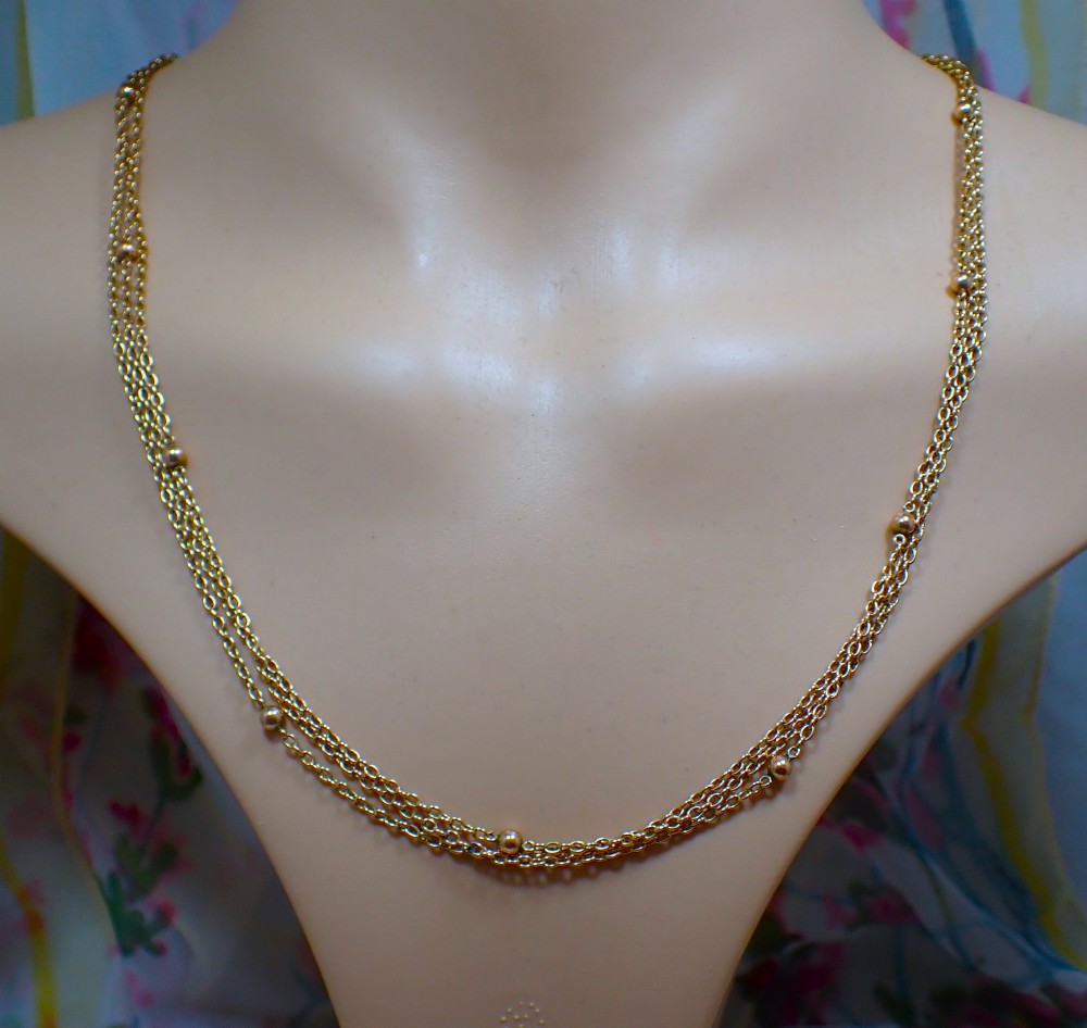 An antique Edwardian 15ct yellow gold guard chain coiled in a spiral, featuring small polished gold beads spaced along trace links and a spring ring clasp. View II