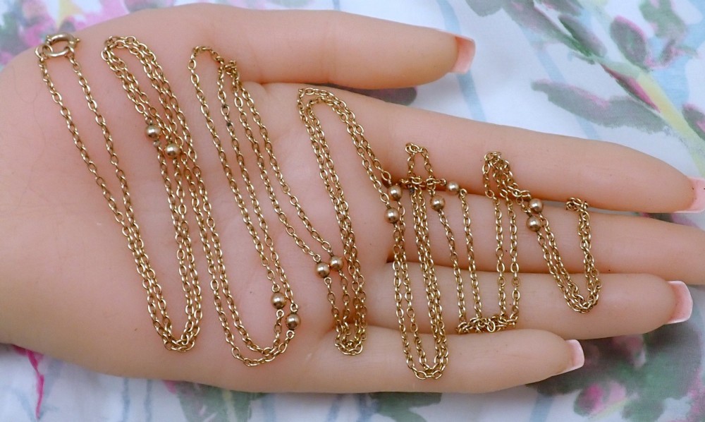 An antique Edwardian 15ct yellow gold guard chain coiled in a spiral, featuring small polished gold beads spaced along trace links and a spring ring clasp. View IV