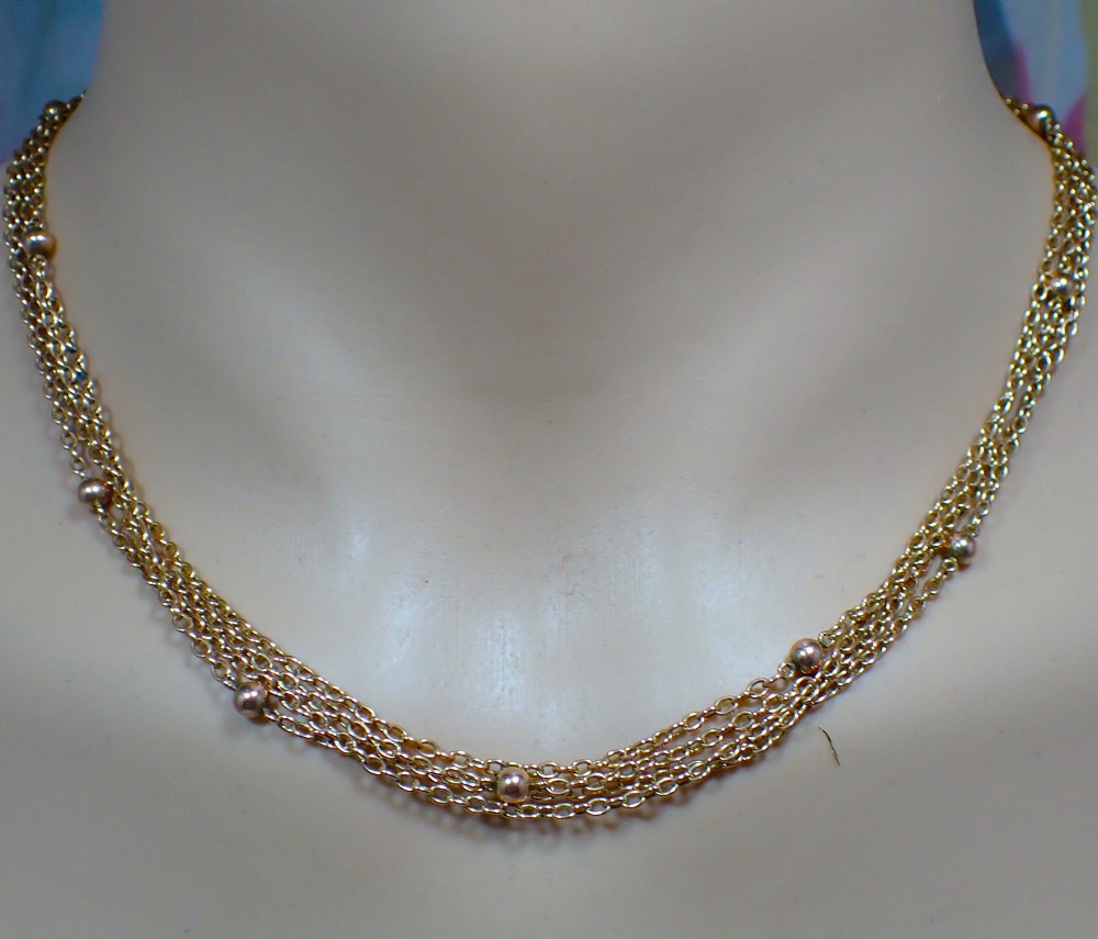 An antique Edwardian 15ct yellow gold guard chain coiled in a spiral, featuring small polished gold beads spaced along trace links and a spring ring clasp. View VI