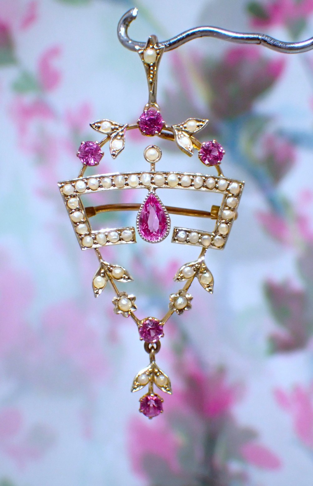 An Edwardian 15ct gold openwork pendant brooch set with natural pink tourmalines and seed pearls, featuring a central pear-cut gemstone drop.