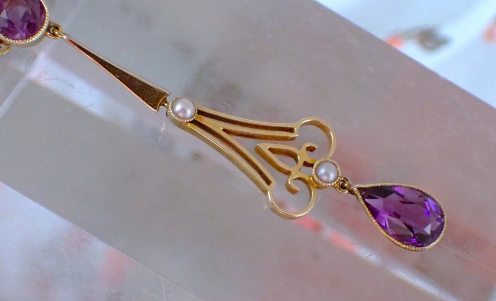 An Art Nouveau 15ct gold pendant featuring openwork scrolling metalwork set with a round amethyst at the top, two seed pearls, and a pear-cut amethyst drop suspended from a fine chain. View III