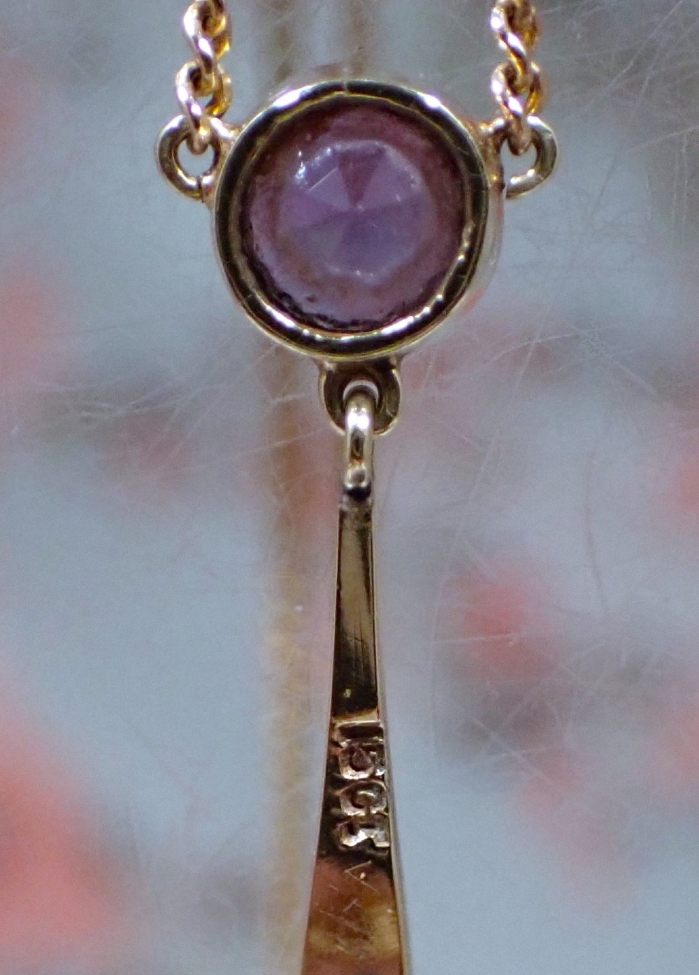 An Art Nouveau 15ct gold pendant featuring openwork scrolling metalwork set with a round amethyst at the top, two seed pearls, and a pear-cut amethyst drop suspended from a fine chain. View VI