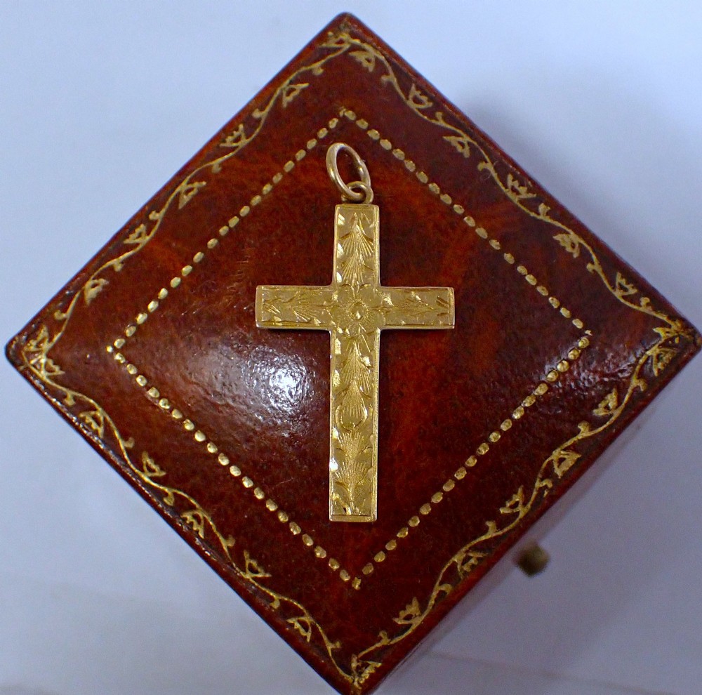 A Victorian 15ct yellow gold cross pendant featuring hand-engraved foliate patterns and a suspension ring at the top.