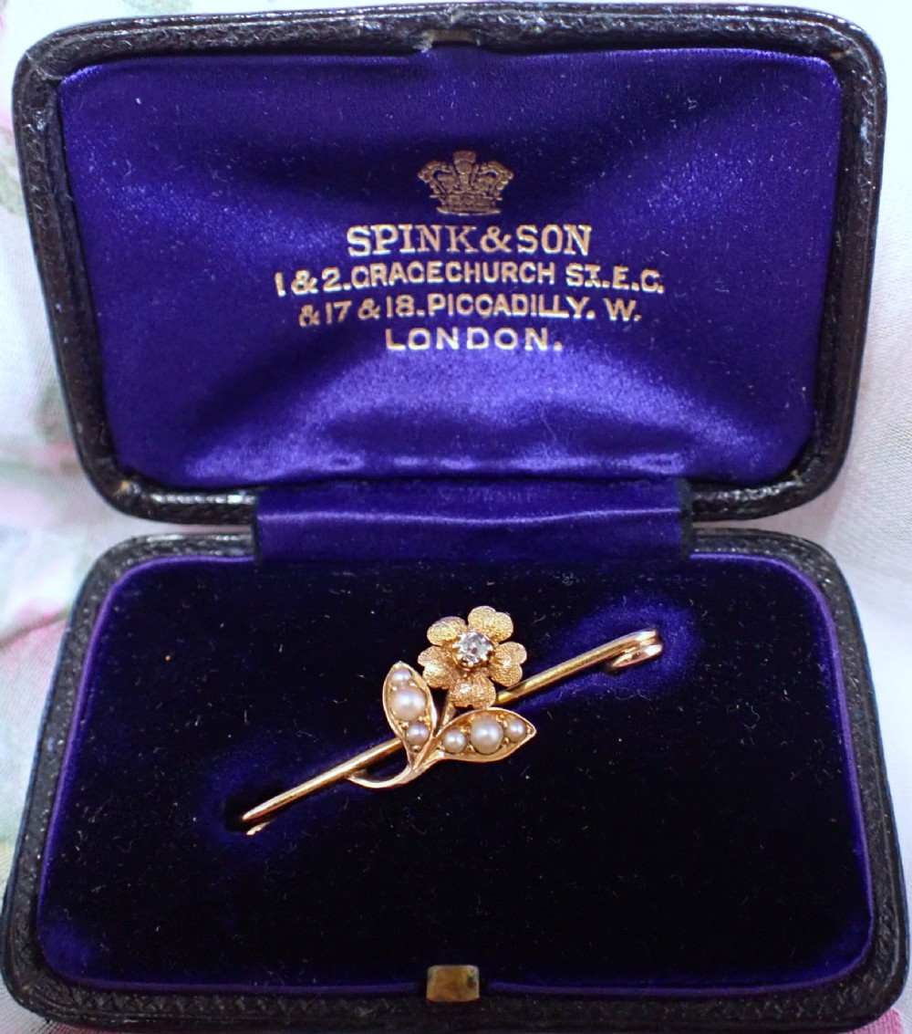 A Victorian 15ct gold bar brooch featuring a central textured flower set with a diamond and foliage set with seed pearls.