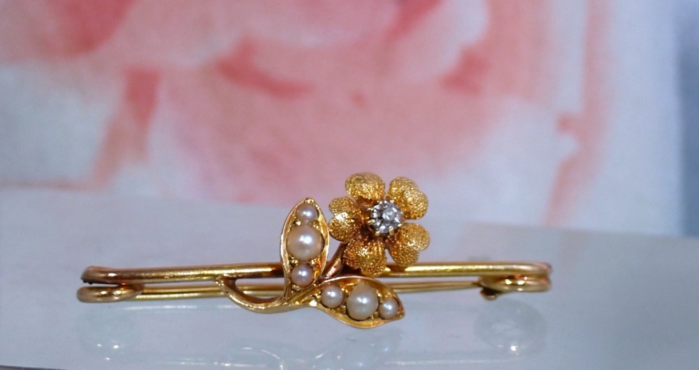 A Victorian 15ct gold bar brooch featuring a central textured flower set with a diamond and foliage set with seed pearls. View III