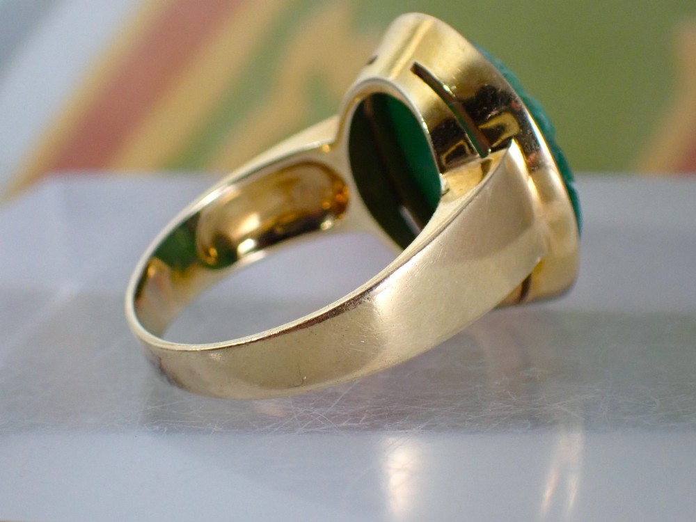 A mid-century yellow gold ring featuring a smooth bezel setting holding an oval carved green jadeite gemstone with floral detail. View III