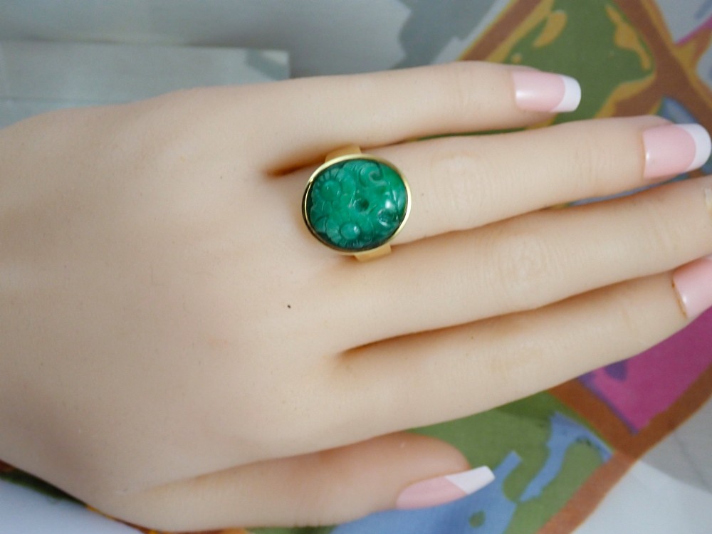 A mid-century yellow gold ring featuring a smooth bezel setting holding an oval carved green jadeite gemstone with floral detail. View IV