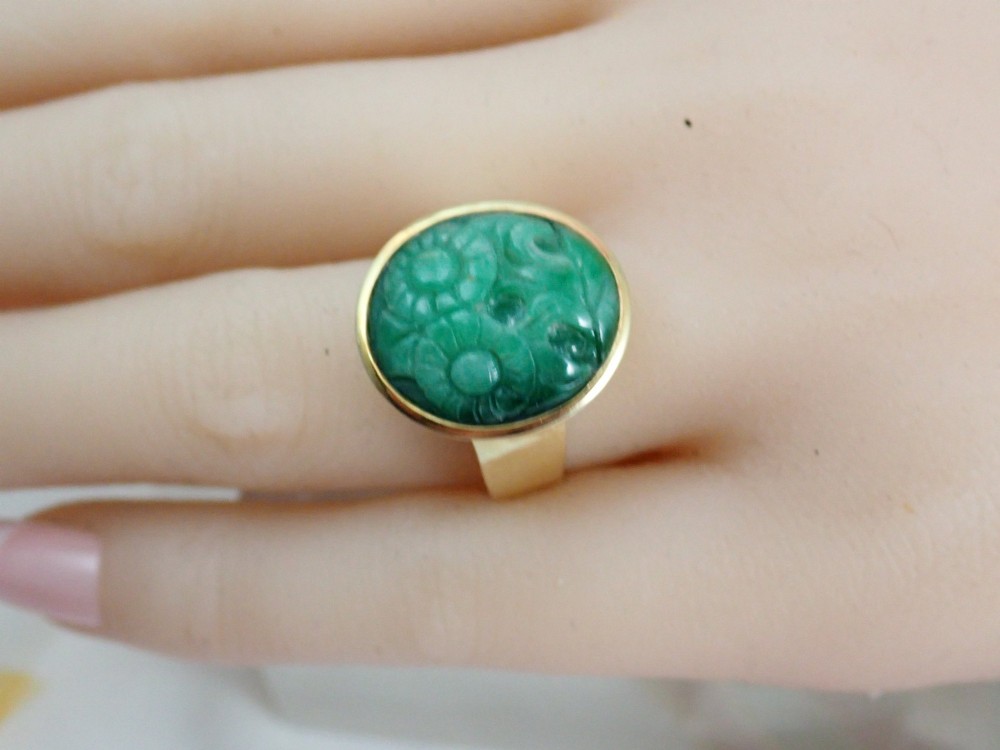 A mid-century yellow gold ring featuring a smooth bezel setting holding an oval carved green jadeite gemstone with floral detail. View VII