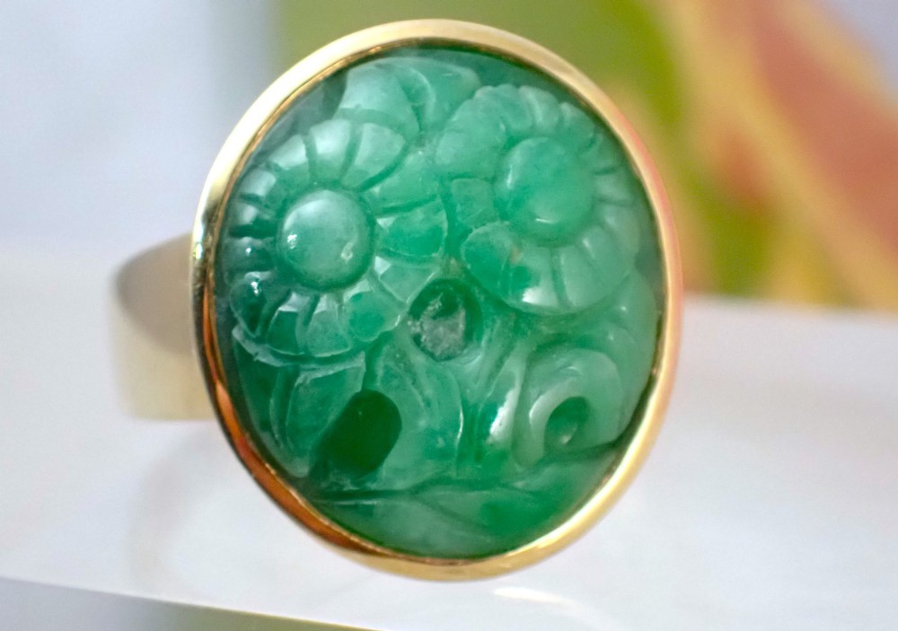 A mid-century yellow gold ring featuring a smooth bezel setting holding an oval carved green jadeite gemstone with floral detail. View VIII