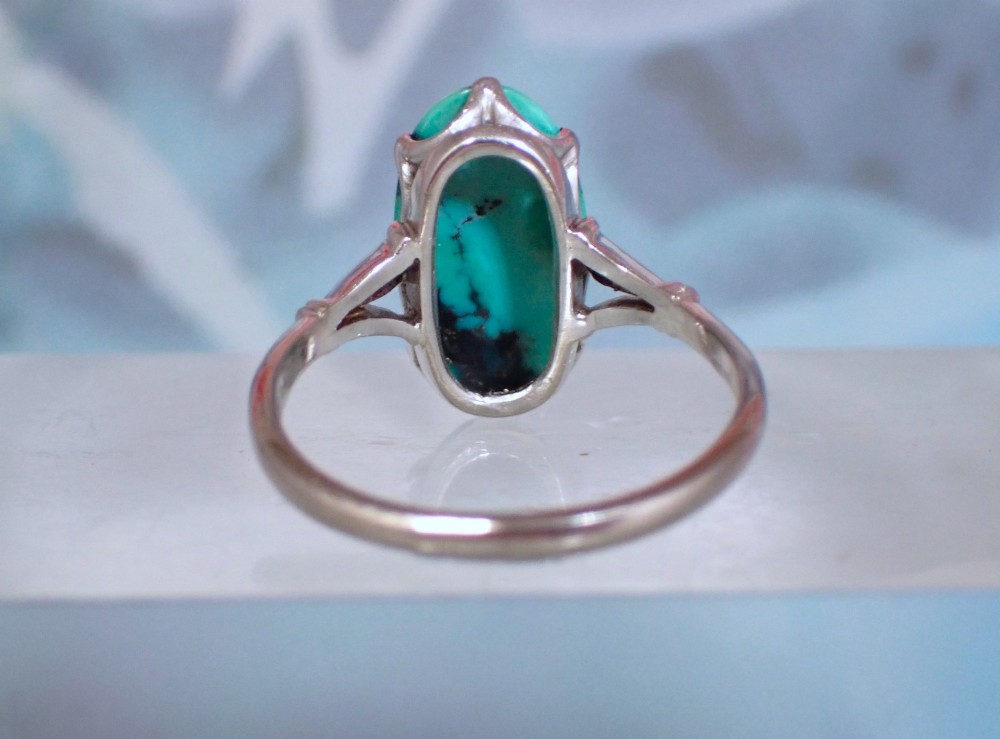 An Art Deco 18ct white gold ring featuring a central oval turquoise cabochon with natural dark matrix patterning, held by claw settings above decorative pierced shoulders. View III