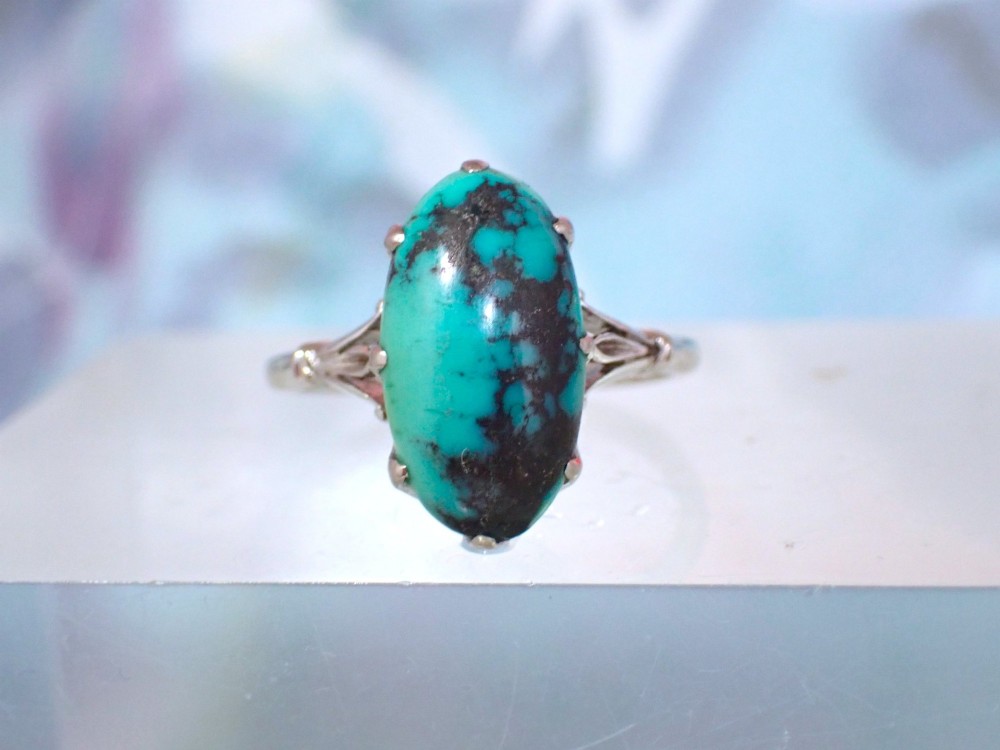 An Art Deco 18ct white gold ring featuring a central oval turquoise cabochon with natural dark matrix patterning, held by claw settings above decorative pierced shoulders. View IV