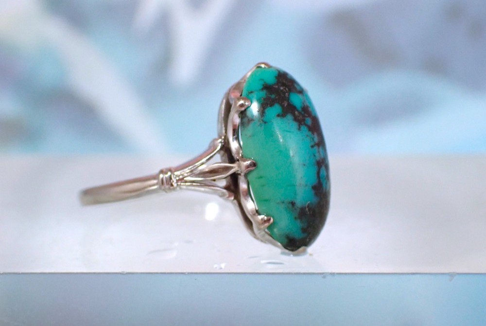 An Art Deco 18ct white gold ring featuring a central oval turquoise cabochon with natural dark matrix patterning, held by claw settings above decorative pierced shoulders. View V