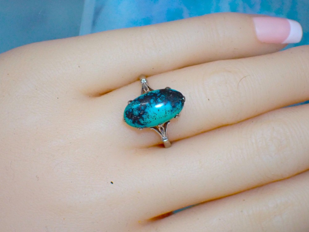 An Art Deco 18ct white gold ring featuring a central oval turquoise cabochon with natural dark matrix patterning, held by claw settings above decorative pierced shoulders. View VI