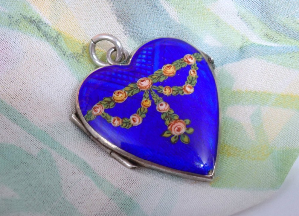 A heart-shaped silver locket featuring cobalt blue guilloche enamel decorated with a hand-painted floral rose garland motif.
