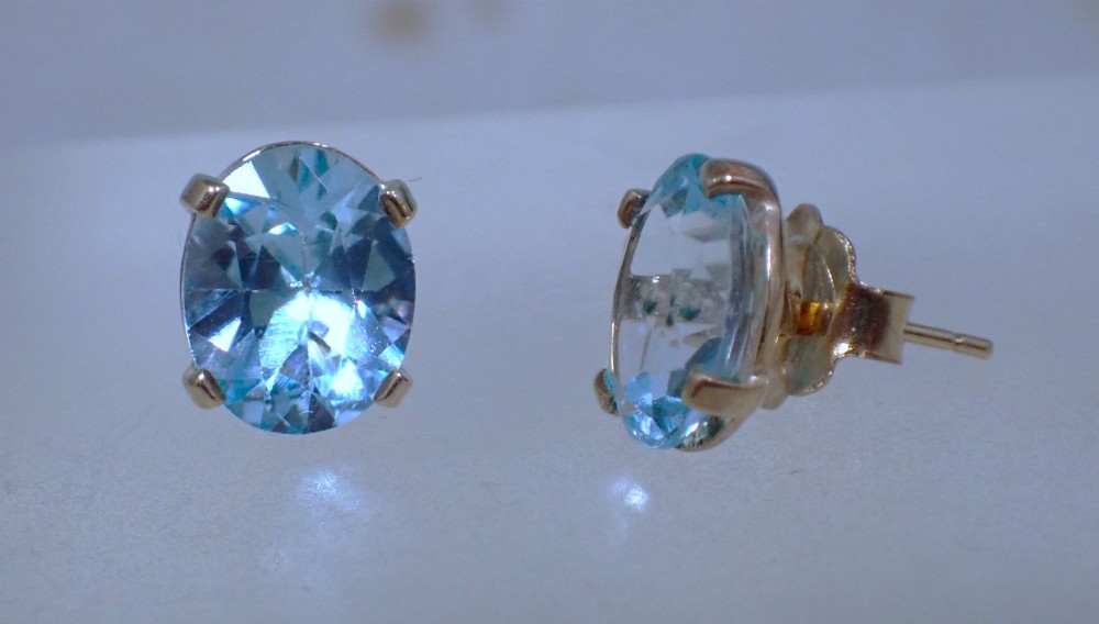 A pair of vintage gold stud earrings featuring oval-cut light blue aquamarine gemstones held within four-prong claw settings. View II