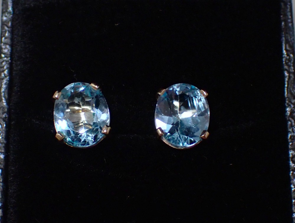 A pair of vintage gold stud earrings featuring oval-cut light blue aquamarine gemstones held within four-prong claw settings. View III