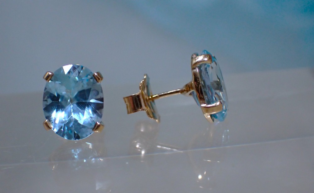 A pair of vintage gold stud earrings featuring oval-cut light blue aquamarine gemstones held within four-prong claw settings. View V