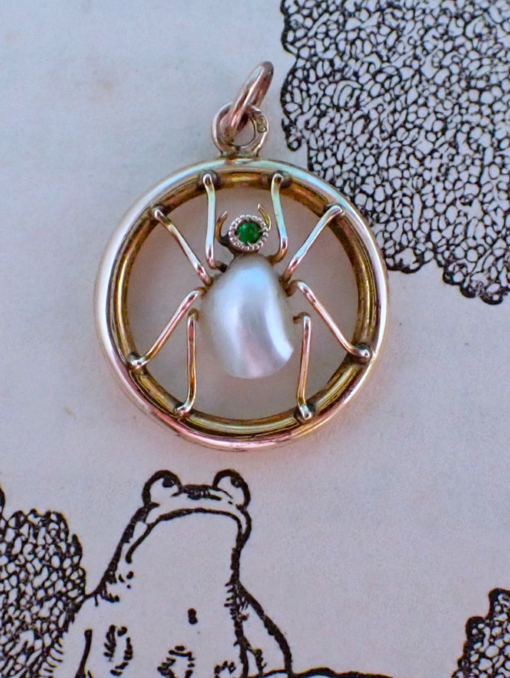 A circular 9ct gold pendant framing a central spider motif set with a pearl abdomen and a small round emerald head. View III