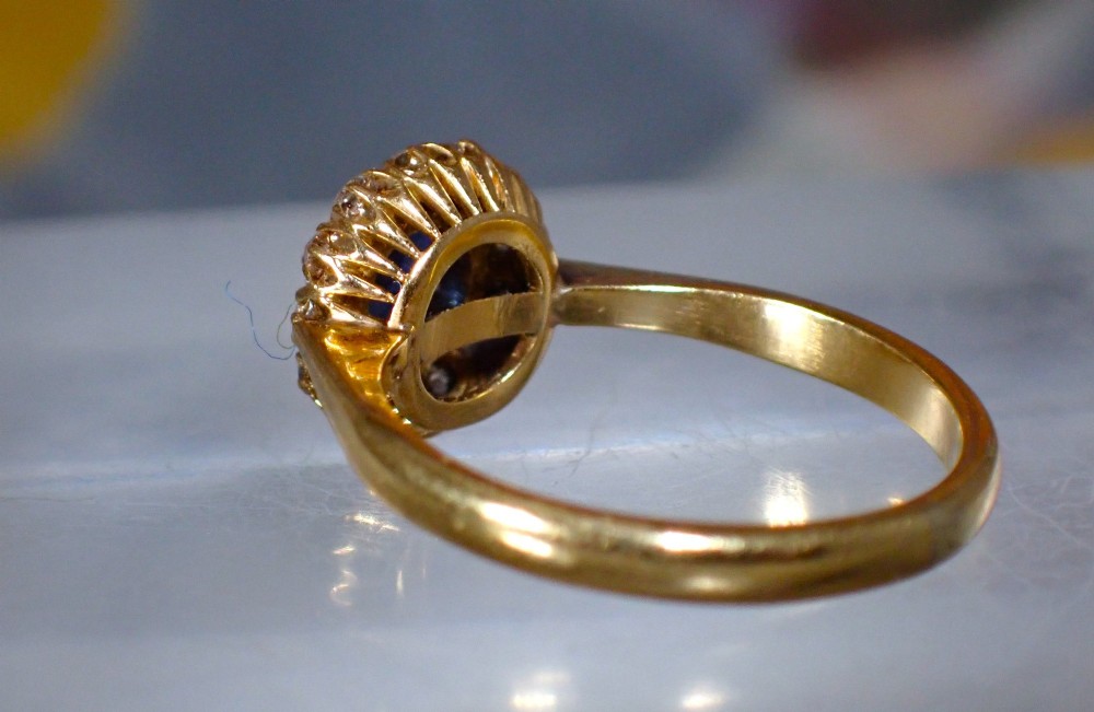 An Edwardian 18ct yellow gold ring featuring a central round blue sapphire surrounded by a floral halo of small diamonds. View VIII