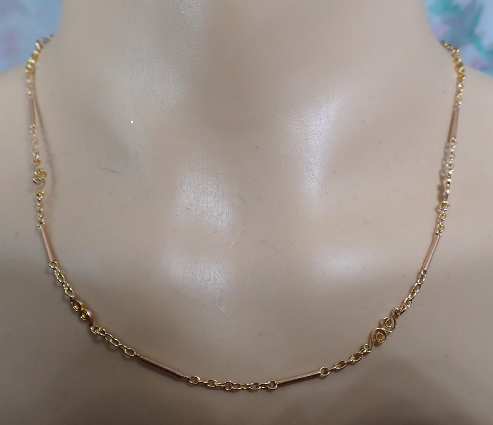 An antique Victorian 9ct rose gold chain composed of alternating cylindrical bar links and coiled wirework scrolls. View V
