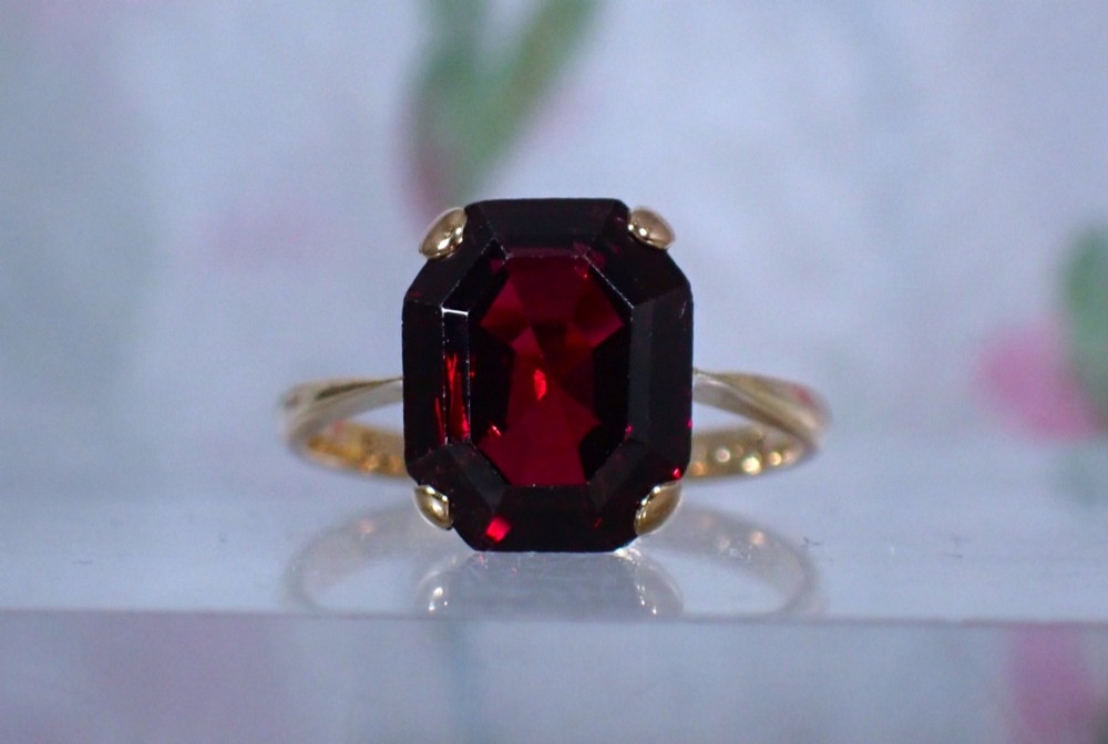 An Art Deco style 9ct yellow gold ring featuring a large, rectangular emerald-cut deep red garnet held by four corner prongs on a slender gold band.
