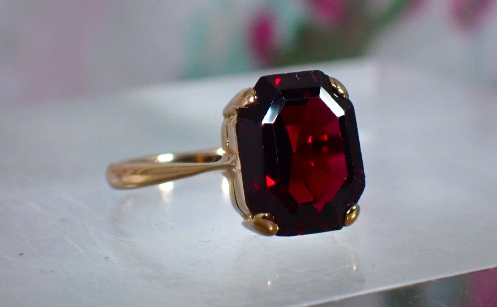 An Art Deco style 9ct yellow gold ring featuring a large, rectangular emerald-cut deep red garnet held by four corner prongs on a slender gold band. View II