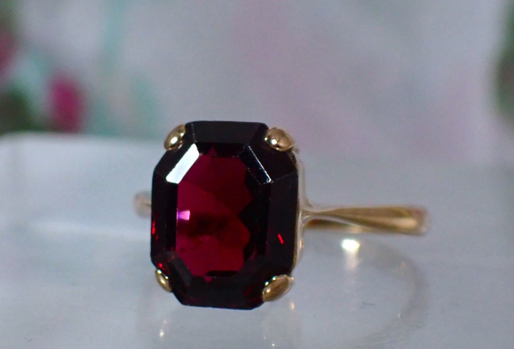 An Art Deco style 9ct yellow gold ring featuring a large, rectangular emerald-cut deep red garnet held by four corner prongs on a slender gold band. View III