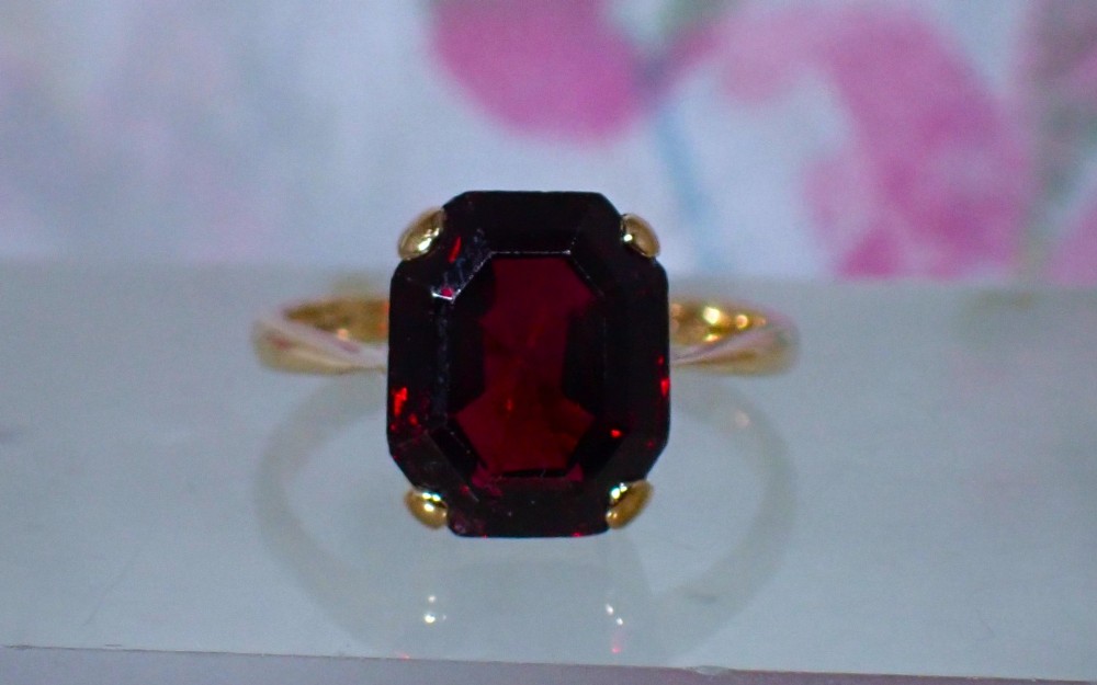 An Art Deco style 9ct yellow gold ring featuring a large, rectangular emerald-cut deep red garnet held by four corner prongs on a slender gold band. View IV