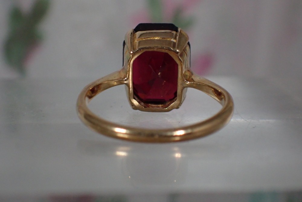 An Art Deco style 9ct yellow gold ring featuring a large, rectangular emerald-cut deep red garnet held by four corner prongs on a slender gold band. View V