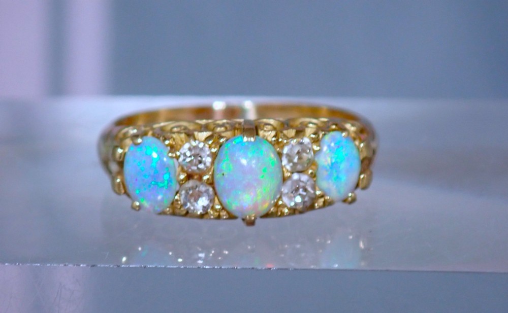 An Edwardian 18ct yellow gold ring set with three oval cabochon opals and small accent diamonds in a carved gallery.