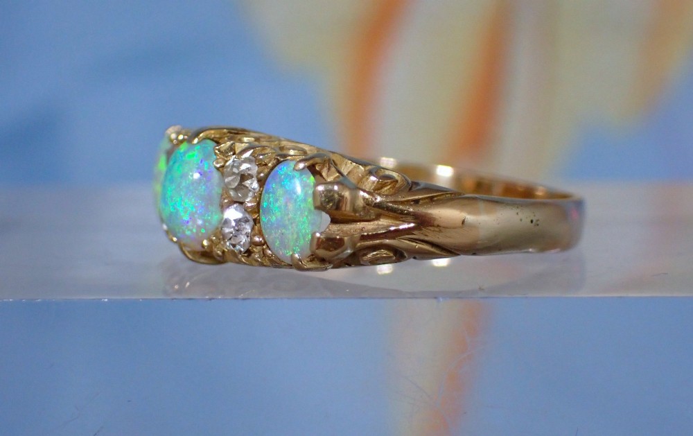 An Edwardian 18ct yellow gold ring set with three oval cabochon opals and small accent diamonds in a carved gallery. View II
