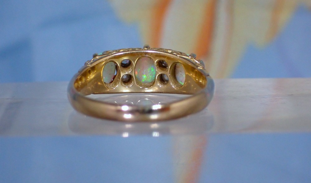 An Edwardian 18ct yellow gold ring set with three oval cabochon opals and small accent diamonds in a carved gallery. View IV