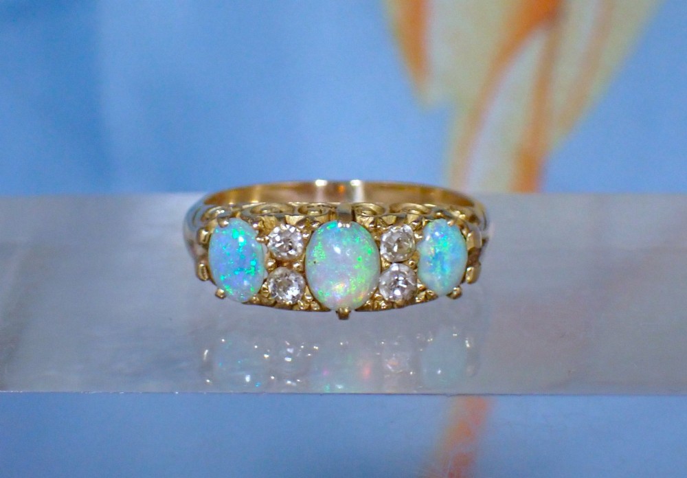 An Edwardian 18ct yellow gold ring set with three oval cabochon opals and small accent diamonds in a carved gallery. View V