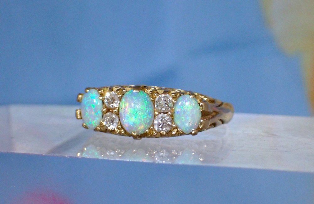 An Edwardian 18ct yellow gold ring set with three oval cabochon opals and small accent diamonds in a carved gallery. View VI