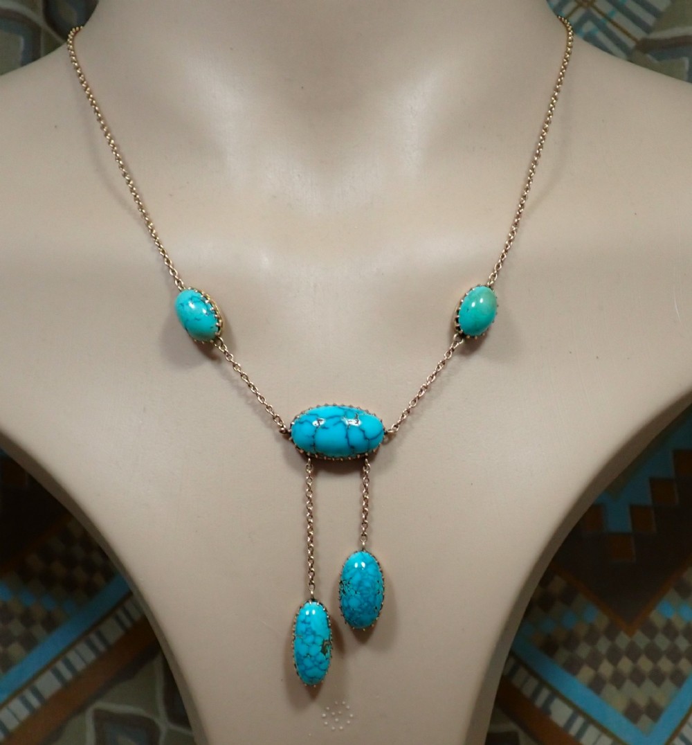 An Edwardian 9ct rose gold negligee necklace set with five oval matrix turquoise cabochons suspended on fine trace chains.