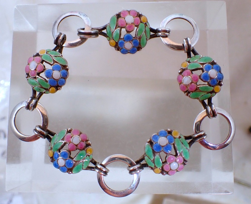 An Arts and Crafts sterling silver link bracelet featuring circular openwork panels decorated with colourful enamelled flowers and leaves.