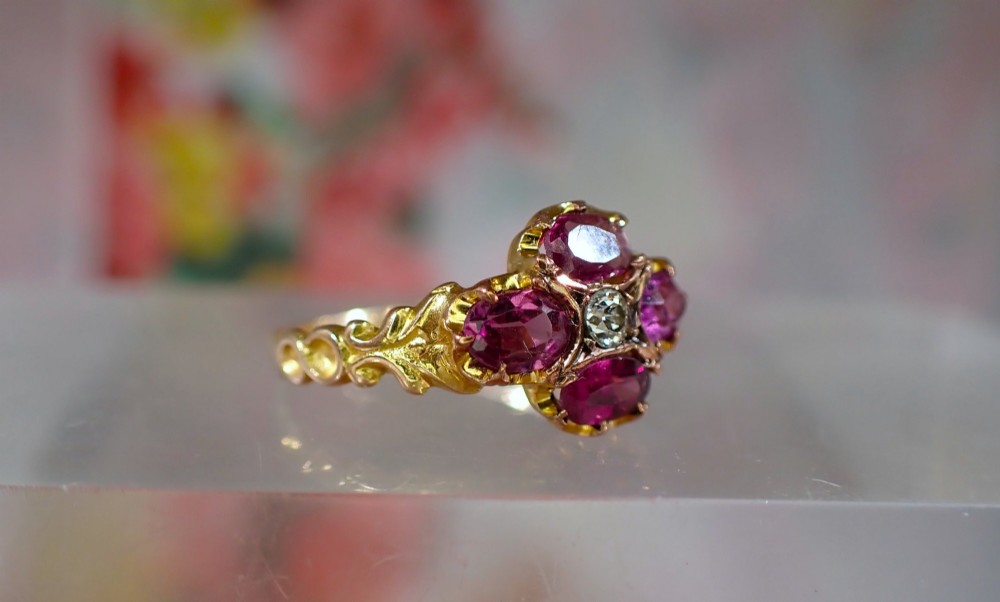 An antique Victorian 15ct yellow gold ring featuring four oval almandine garnets centred around a single old-cut diamond with carved scroll shoulders. View II